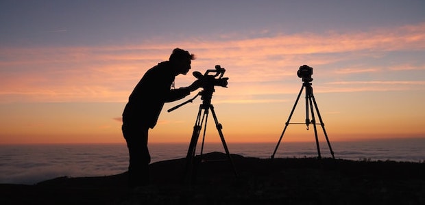 Ein Mann filmt den Sonnenuntergang mit einer Kamera auf einem Stativ.